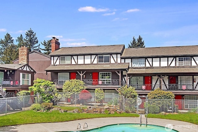 back of house with a chimney, a shingled roof, and fence