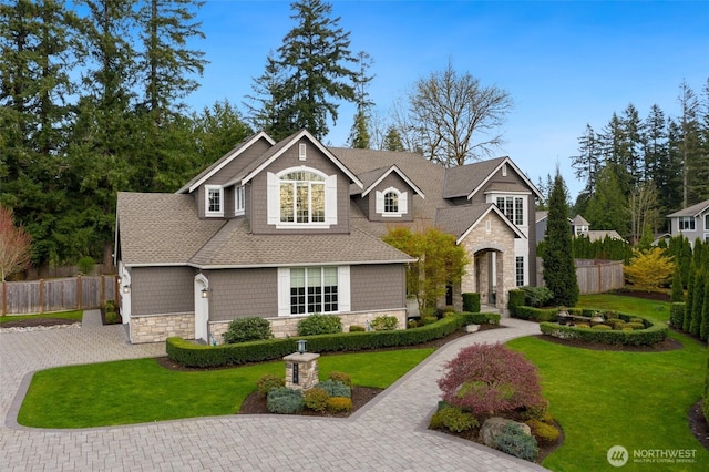 view of front of property with roof with shingles, fence, stone siding, a front lawn, and driveway