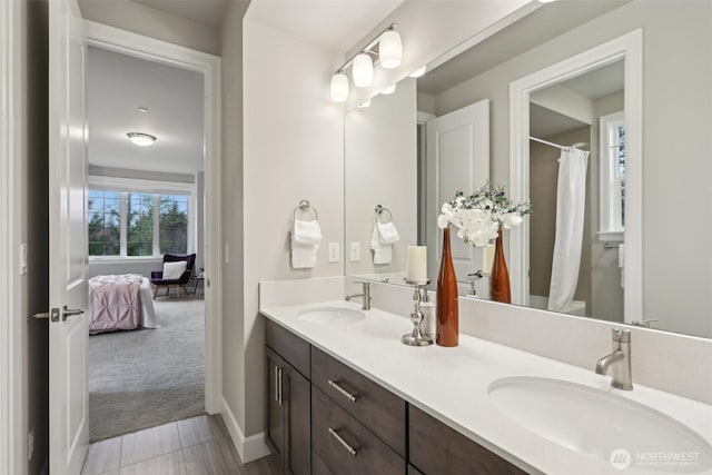 ensuite bathroom featuring a sink, baseboards, double vanity, and a shower with curtain