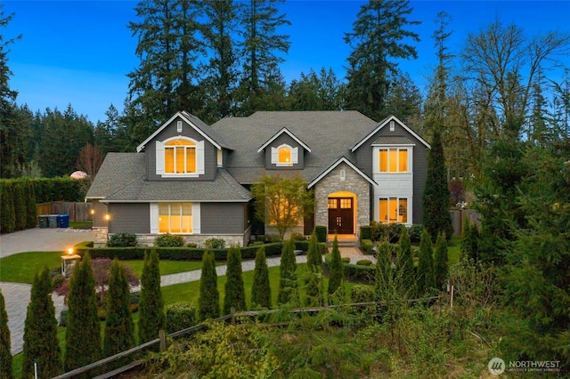 view of front facade with a shingled roof, fence, and stone siding