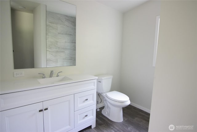 bathroom with toilet, vanity, baseboards, and wood finished floors