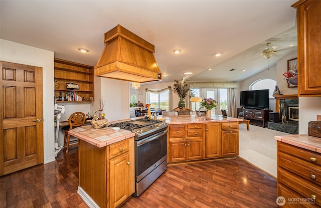 kitchen with custom exhaust hood, tile counters, stainless steel range with gas stovetop, a ceiling fan, and open floor plan