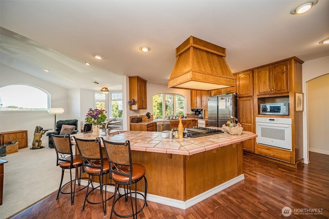 kitchen featuring appliances with stainless steel finishes, tile countertops, a breakfast bar area, dark wood-style floors, and brown cabinetry
