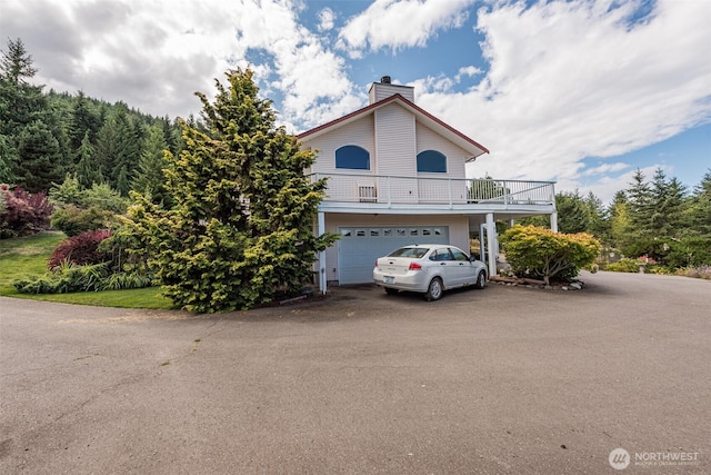 view of front of house with a balcony, a chimney, an attached garage, and aphalt driveway