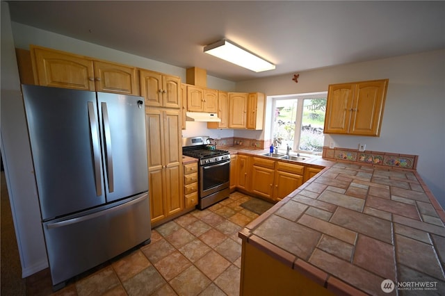 kitchen with stainless steel appliances, under cabinet range hood, a sink, tile countertops, and a peninsula
