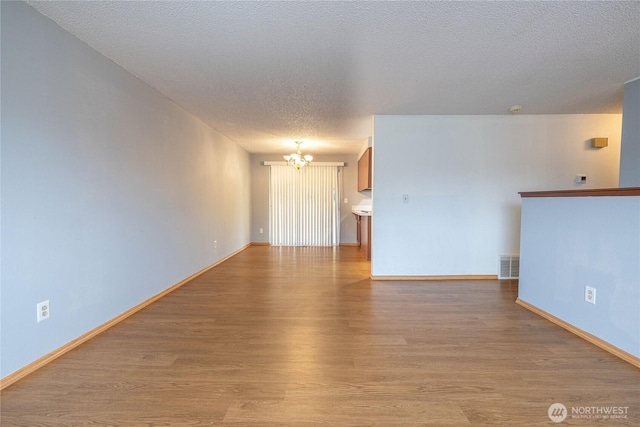 1023 S 88th St, Tacoma, WA 98444 - unfurnished living room featuring a notable chandelier, baseboards, a textured ceiling, visible vents, and light wood finished floors