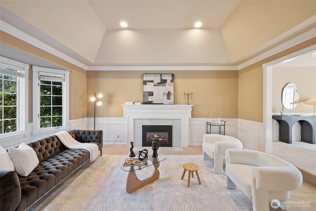 living area featuring a decorative wall, wainscoting, a high end fireplace, and lofted ceiling