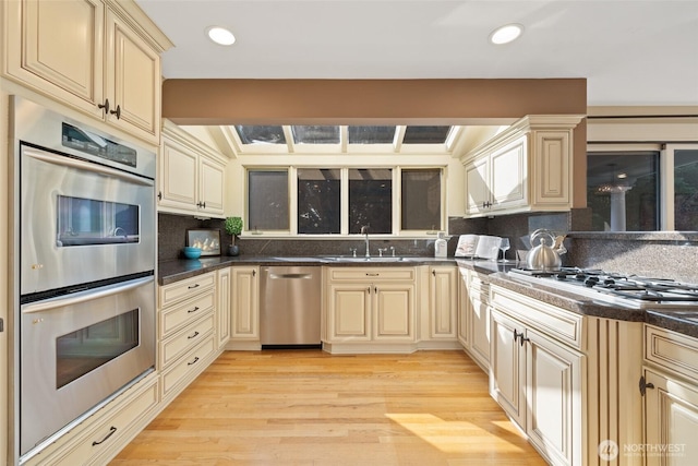 kitchen with stainless steel appliances, a sink, backsplash, and cream cabinetry