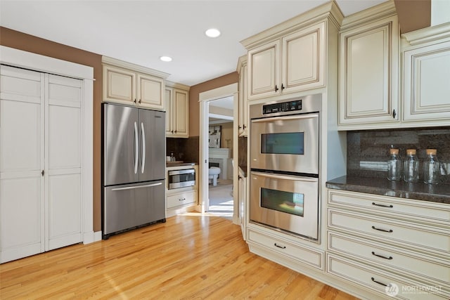 kitchen with light wood-style flooring, tasteful backsplash, stainless steel appliances, and cream cabinetry