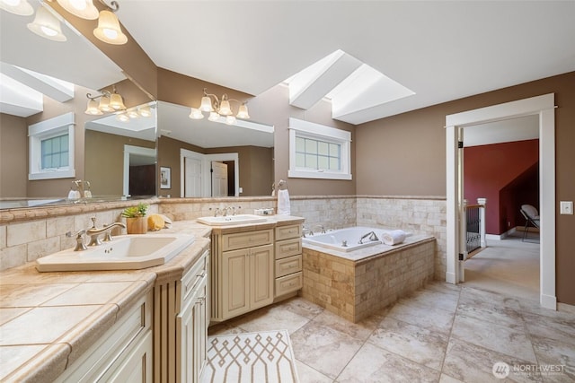 full bathroom with vanity, a skylight, a notable chandelier, and a garden tub