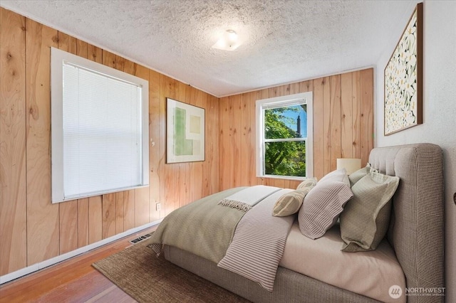 8434 34th Ave S, Seattle, WA 98118 - bedroom featuring wooden walls, wood finished floors, a textured ceiling, and baseboards