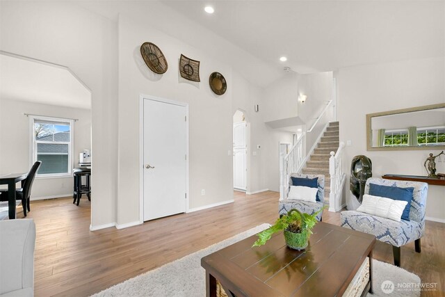 living room with light wood-style flooring, stairway, arched walkways, and baseboards