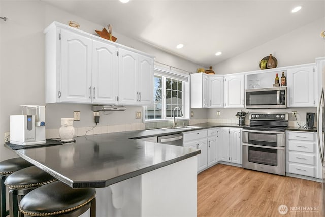 kitchen featuring a peninsula, dark countertops, a sink, and stainless steel appliances