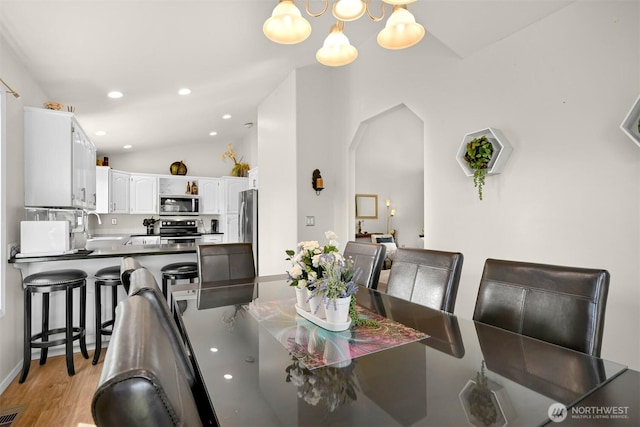 dining space with vaulted ceiling, a chandelier, recessed lighting, light wood-style flooring, and arched walkways