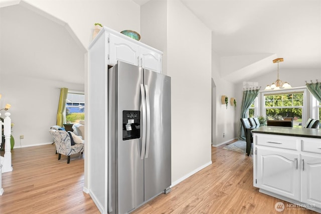 kitchen with vaulted ceiling, stainless steel fridge, white cabinetry, dark countertops, and light wood-style floors