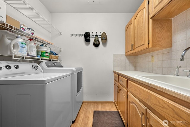 clothes washing area with a sink, light wood finished floors, baseboards, cabinet space, and washer and clothes dryer