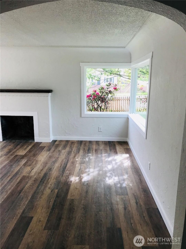 201 S 60th St, Tacoma, WA 98408 - unfurnished living room with baseboards, a textured ceiling, a fireplace with flush hearth, arched walkways, and wood-type flooring