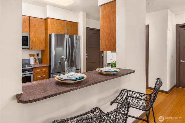 413 NE 70th St Unit 402, Seattle, WA 98115 - kitchen featuring baseboards, wood finished floors, stainless steel appliances, dark countertops, and brown cabinets