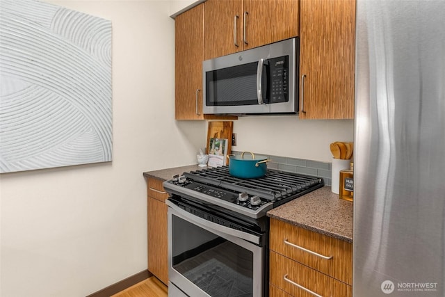 413 NE 70th St Unit 402, Seattle, WA 98115 - kitchen with baseboards, dark stone countertops, brown cabinetry, and appliances with stainless steel finishes