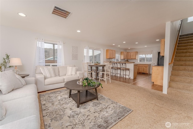 living room with a healthy amount of sunlight, recessed lighting, visible vents, and stairway