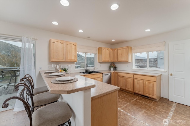 kitchen with a kitchen breakfast bar, light brown cabinets, light countertops, stainless steel dishwasher, and a sink