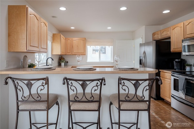 kitchen featuring a peninsula, appliances with stainless steel finishes, a breakfast bar, and light brown cabinetry