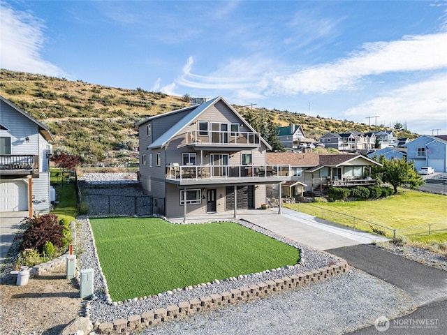view of front of house featuring concrete driveway, a balcony, fence, and a front lawn