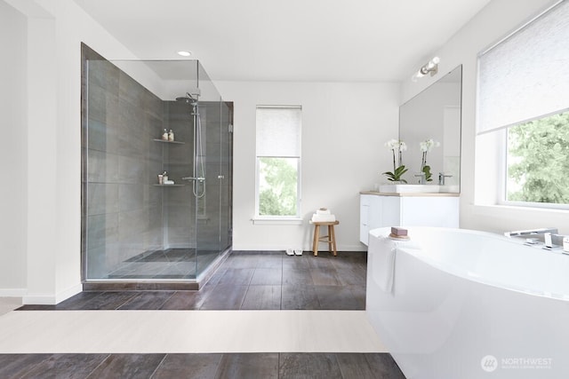 full bath featuring baseboards, a freestanding tub, a shower stall, vanity, and wood finished floors