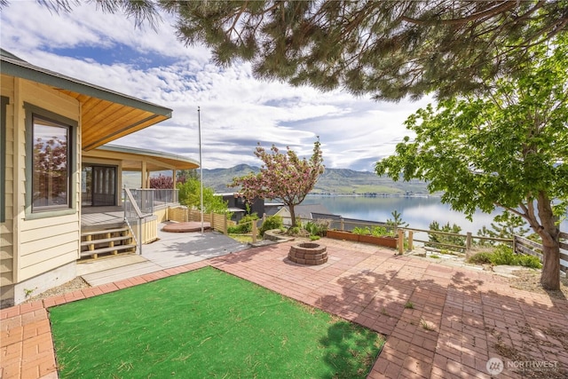 view of yard with an outdoor fire pit, a patio area, a deck with water view, and fence