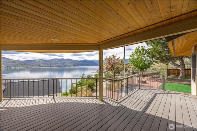 wooden terrace featuring a water and mountain view, fence, and a patio
