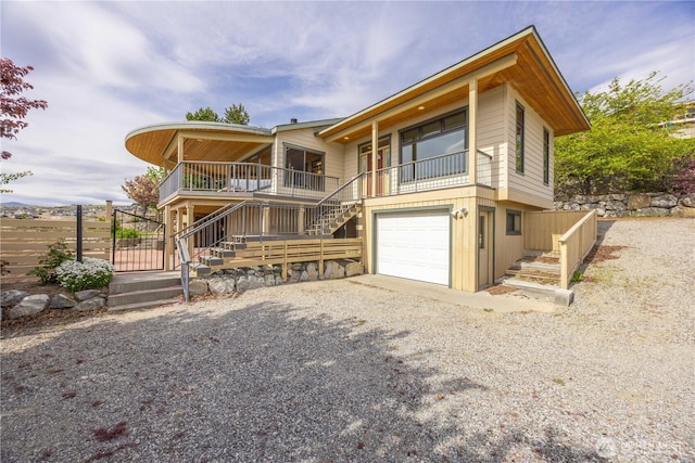 view of front of house with fence, a garage, stairway, covered porch, and gravel driveway
