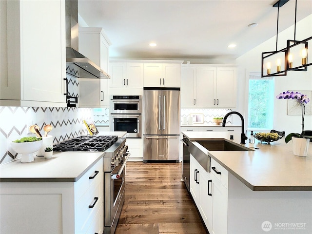 kitchen featuring high quality appliances, wood finished floors, a sink, white cabinets, and wall chimney exhaust hood