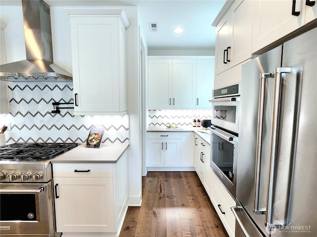 kitchen featuring light countertops, wall chimney exhaust hood, decorative backsplash, premium appliances, and visible vents