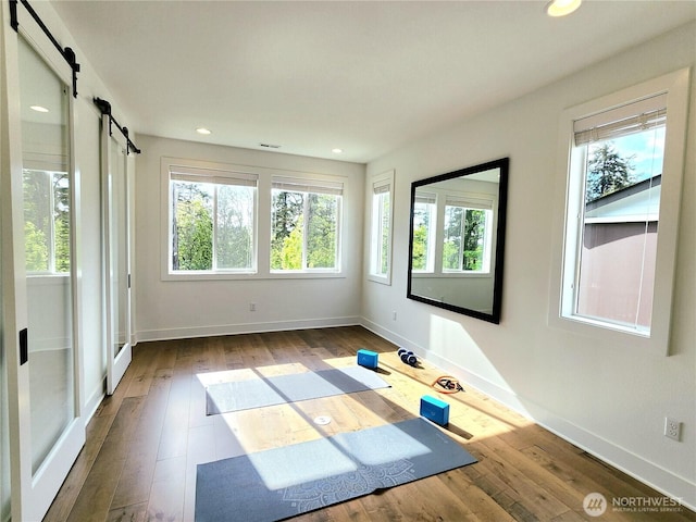 exercise area featuring recessed lighting, baseboards, a barn door, and hardwood / wood-style flooring
