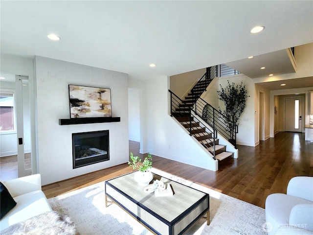 living area with a tiled fireplace, recessed lighting, stairs, and wood finished floors