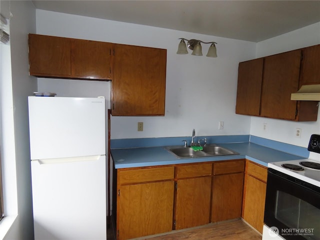 kitchen featuring a sink, under cabinet range hood, electric range oven, brown cabinetry, and freestanding refrigerator