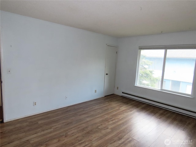 empty room featuring wood finished floors and baseboard heating