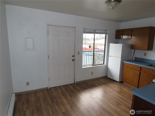 kitchen with a baseboard heating unit, brown cabinetry, freestanding refrigerator, and wood finished floors