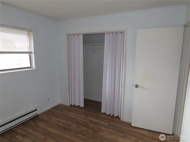 unfurnished bedroom featuring wood finished floors, a baseboard heating unit, and a closet