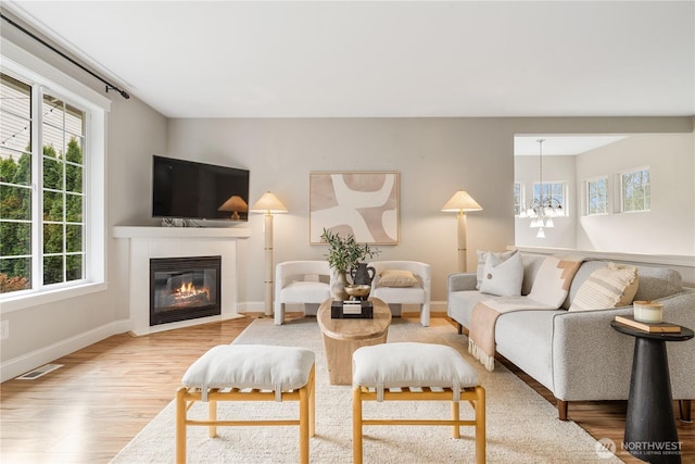 living area featuring wood finished floors, a tile fireplace, a chandelier, baseboards, and visible vents