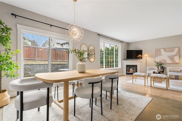 dining area with a glass covered fireplace, a notable chandelier, and light wood-type flooring