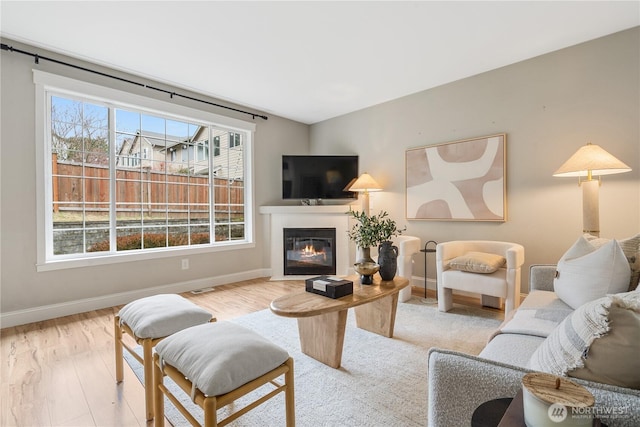 living room featuring baseboards, wood finished floors, and a fireplace with flush hearth