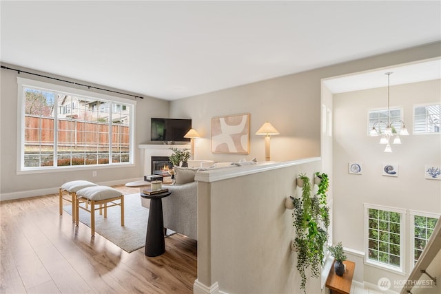 living room with a glass covered fireplace, a notable chandelier, wood finished floors, and baseboards
