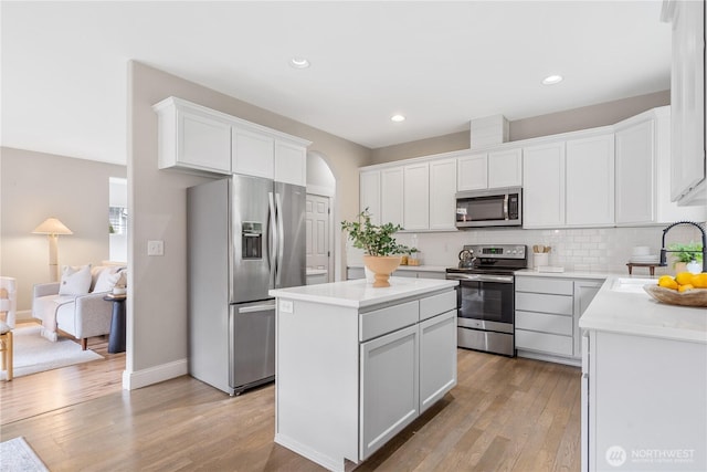 kitchen with a sink, appliances with stainless steel finishes, light wood-style floors, a center island, and backsplash