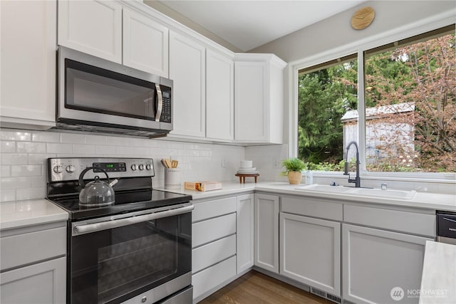 kitchen with white cabinets, a sink, appliances with stainless steel finishes, light countertops, and backsplash