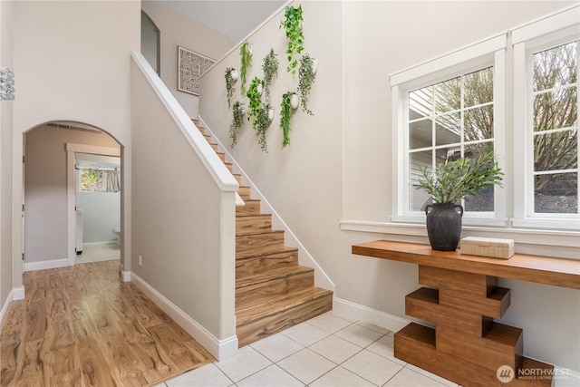 staircase featuring baseboards, arched walkways, and wood finished floors