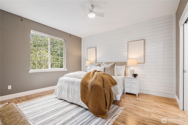 bedroom featuring wooden walls, light wood finished floors, a ceiling fan, and baseboards