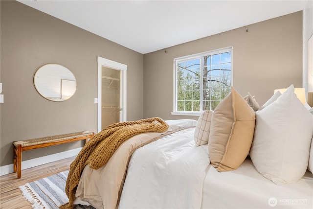 bedroom featuring a closet, a spacious closet, wood finished floors, and baseboards