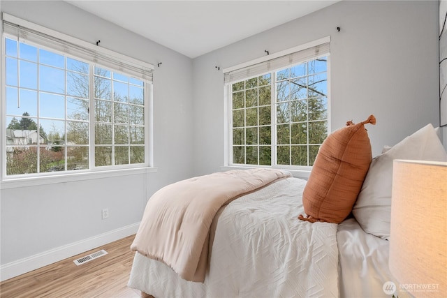 bedroom with baseboards, visible vents, and wood finished floors