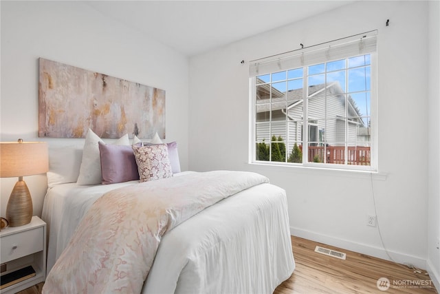 bedroom featuring baseboards, visible vents, wood finished floors, and multiple windows